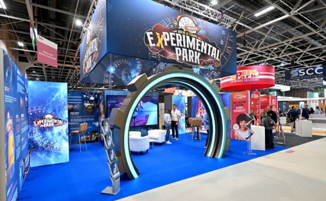 An exhibition stand entitled Experimental Park with a blue light arch, white seats and futuristic decor, featuring interactive entertainment activities.